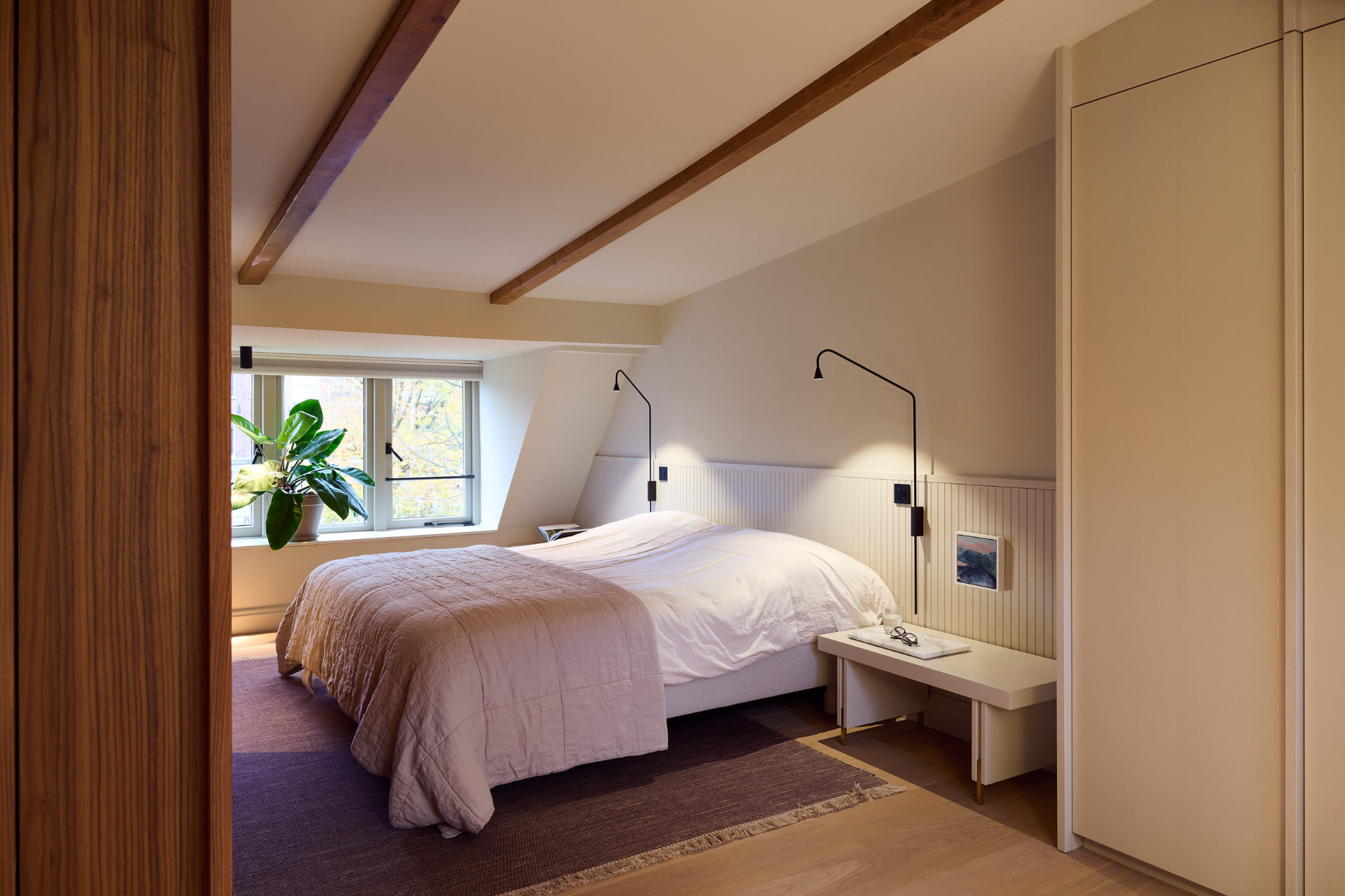 Slaapkamer met houten balken en zicht op groen