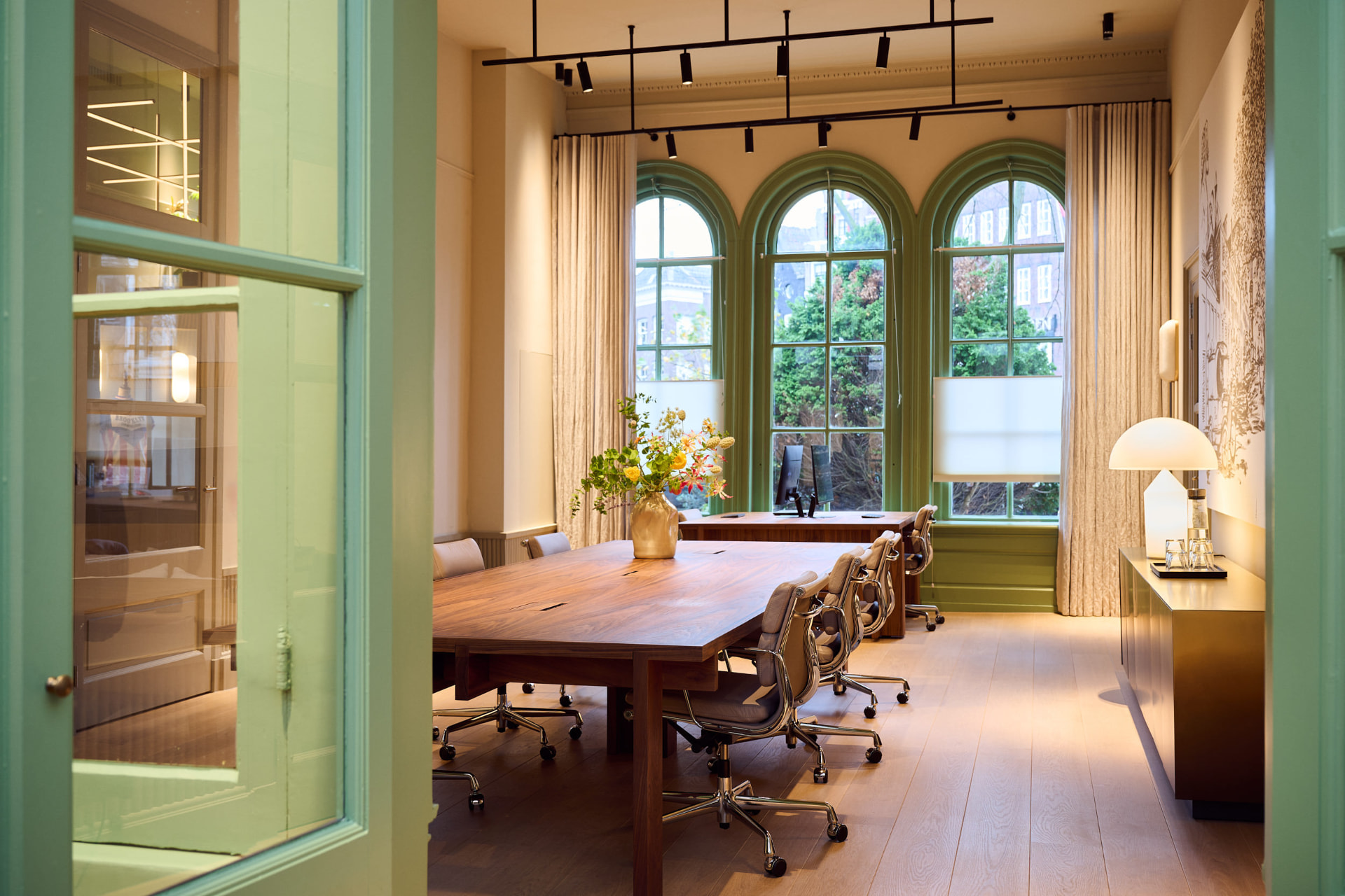 Vergaderruimte met houten tafel en hoge groene ramen